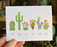 Load image into Gallery viewer, Tucson Flora greeting card, the word &quot;TUCSON&quot; written in all caps handwriting with an assortment of plants painted in watercolor above. Including barrel cactus, saguaro, elf aloe, teddy bear cholla, prickly pear, and torch cactus.