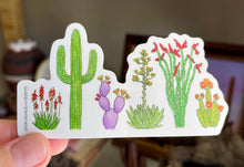 Load image into Gallery viewer, Hand holding a sticker with desert plants design in front of a blurred indoor setting.