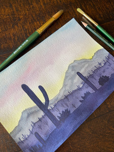 Painting of a desert landscape with cacti on a wooden surface with art supplies.