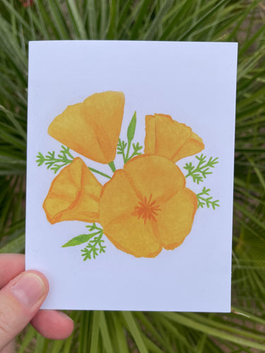 A hand holding a white card with a watercolor illustration of 4 orange poppy flowers with green leaves, on a green leaf background