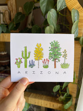 Load image into Gallery viewer, Arizona Flora greeting card, the word &quot;ARIZONA&quot; written in all caps handwriting with an assortment of plants painted in watercolor above. Including prickly pear, saguaro, lupine, aspen, elf aloe, ponderossa pine, and agave.