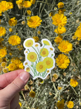 Load image into Gallery viewer, Hand holding a desert marigold sticker with real desert marigold flowers in the background