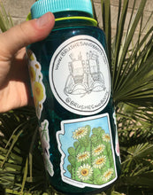 Load image into Gallery viewer, Vinyl sticker in the shape of Arizona with a watercolor painting of the top of a saguaro cactus with white blooming flowers. The sticker is on a water bottle with other stickers by Brushes and Boots.