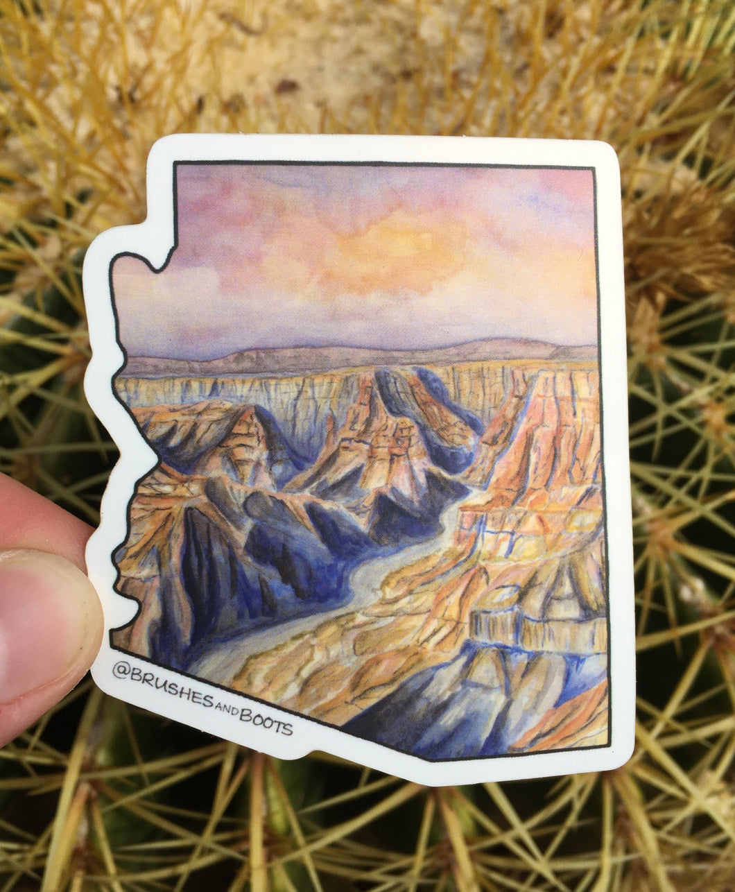Vinyl sticker the shape of Arizona with a watercolor scene of the Grand Canyon at sunset with a pink/purple sky and deep shadows in the canyon with orange sun highlights